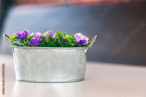 An artificial flower in metal bucket on white table.