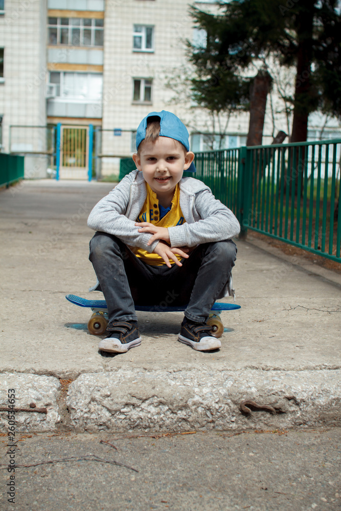 Obraz premium Little city boy with a skateboard. Young guy in a cap sits. Urban style. City kids. Kid's having fun
