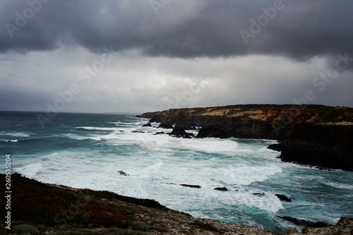 Storm over the sea, dark clouds, large waves, rock formations in the water, cliffs. Alentejo, Portugal 