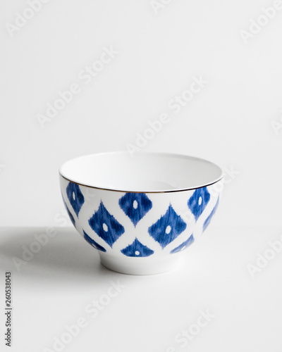 Elegant cutlery front view on a isolated white background. Porcelain soup bowl with blue rhombus and gold edging around the edge. Trendy plate pastel shades. Flat lay view.