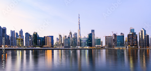 Panoramic view of the illuminated Dubai skyline during sunset with the magnificent Burj Khalifa and many others skyscrapers reflected on a silky smooth water flowing in the foreground. Dubai.