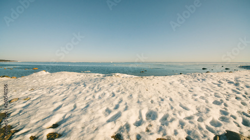 Fototapeta Naklejka Na Ścianę i Meble -  Snow pile on the beach, hill. Large snow drift isolated on a blue sky background,  outdoor view of ice blocks at frozen finland lake in winter
