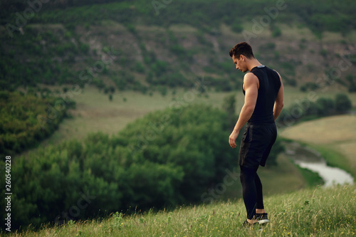 Profile of a athlete, muscular, fit, abs, young man doing stretching exercises before workout outside on forest, river background.