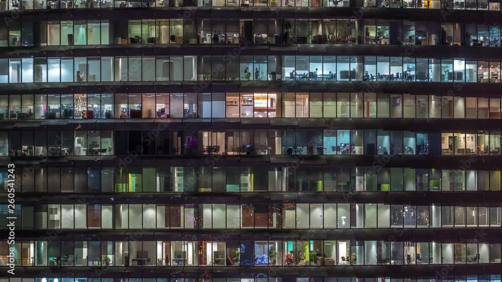 Working evening in glass business centre office building with numerous offices with glass walls and illuminated windows timelapse. People sitting at desks Working evening in glass business centre office building with numerous offices with glass walls and illuminated windows timelapse. People sitting at desks