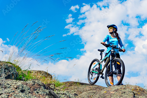 Woman cyclist stands on the hilltop with her mountain bike.