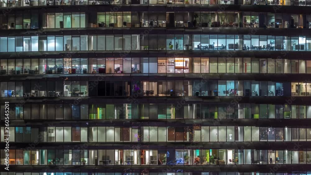 Working evening in glass business centre office building with numerous offices with glass walls and illuminated windows timelapse. People sitting at desks. Pan up Working evening in glass business centre office building with numerous offices with glass walls and illuminated windows timelapse. People sitting at desks. Pan up