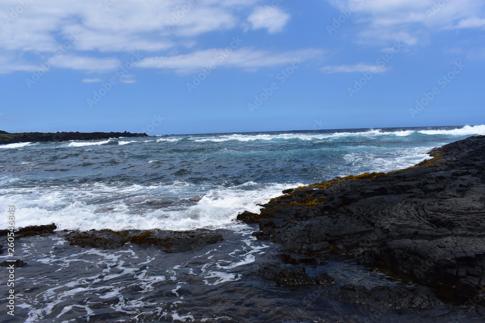 Waves Crashing on Rocky Shore in Hawaii white foam as the waves wash over the rocks under a blue sky