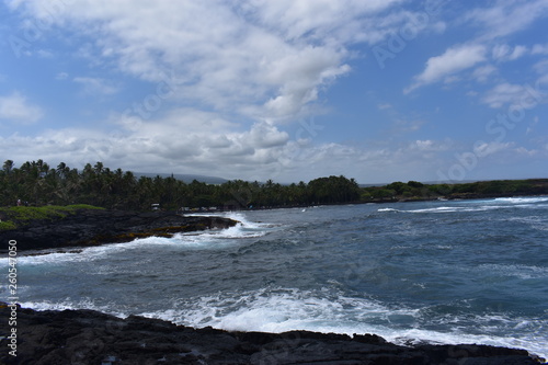 Waves Crashing on Rocky Shore in Hawaii white foam as the waves wash over the rocks under a blue sky