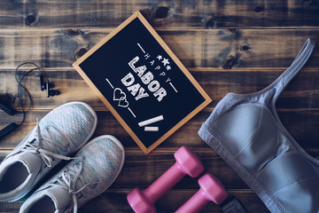 Happy Labor Day Fitness and healthy active lifestyle background concept. Training sneakers, dumbbells, sport bra and headphones on wooden background.
