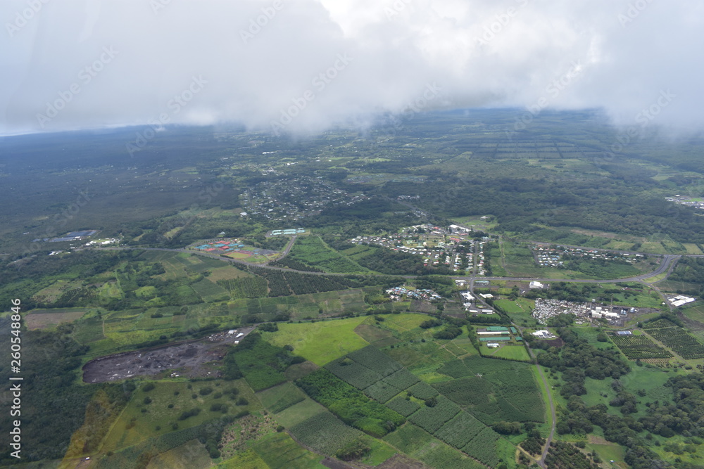 Arial view of Hilo Hawaii with orchards and crops spread far up to heavily populated city. View from a helicopter above the clouds