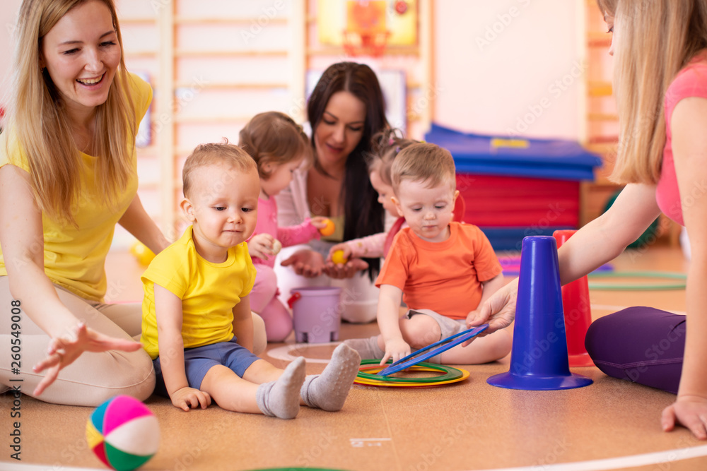 Mothers and their children together in gym. Babies playing with sportive equipment Mothers and their children together in gym. Babies playing with sportive equipment
