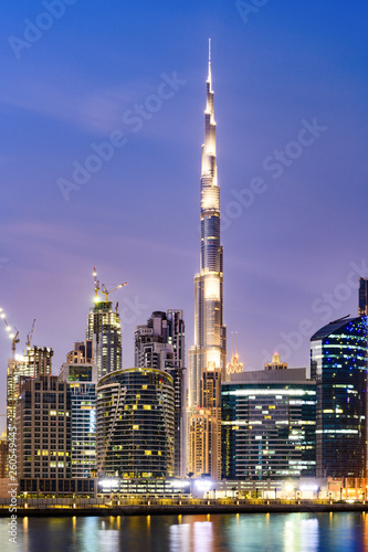 Foto Stunning view of the illuminated Dubai skyline during sunset with the magnificent Burj Khalifa and many other buildings and skyscrapers reflected on a silky smooth water flowing in the foreground