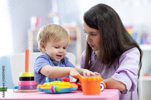 Cute woman with child playing with plastic blocks at home or kindergarten