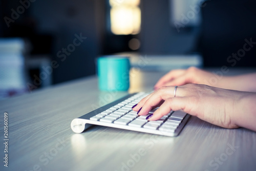 Woman hands with polished nails typing on white wireless keyboard.