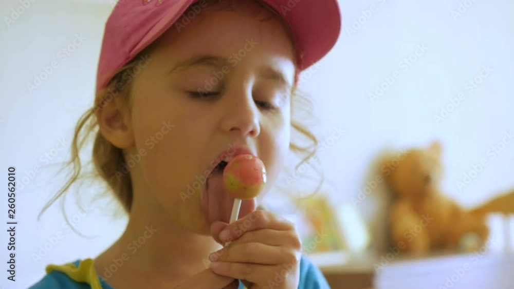 Little girl enjoying a lollipop while staring at camera. Child eating candy, sweets, sugar