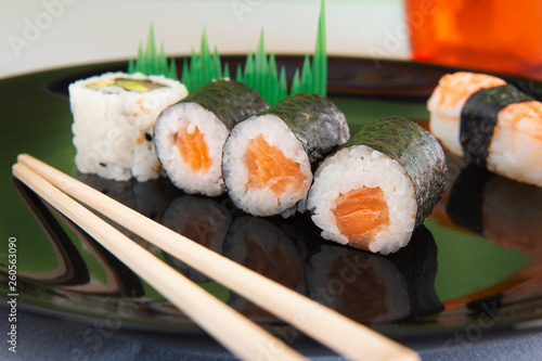 mixed sushi on black plate with orange glass and Japanese chopsticks