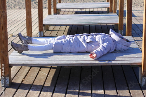 Young woman in  winter jacket sunbathing on sun bed near sea. Winter holidays concept. photo