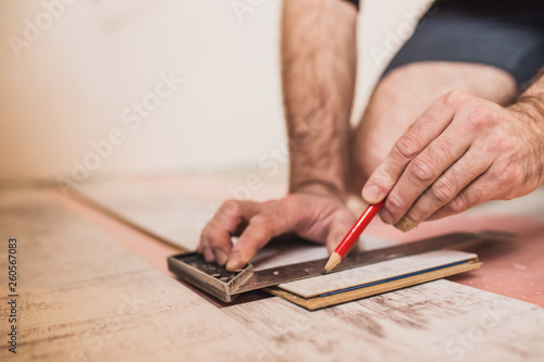 A worker makes a markup with a pencil and a square on the laminate panel for trimming