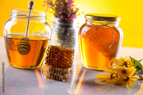 Honey dripping from a wooden honey dipper in a jar on wooden background