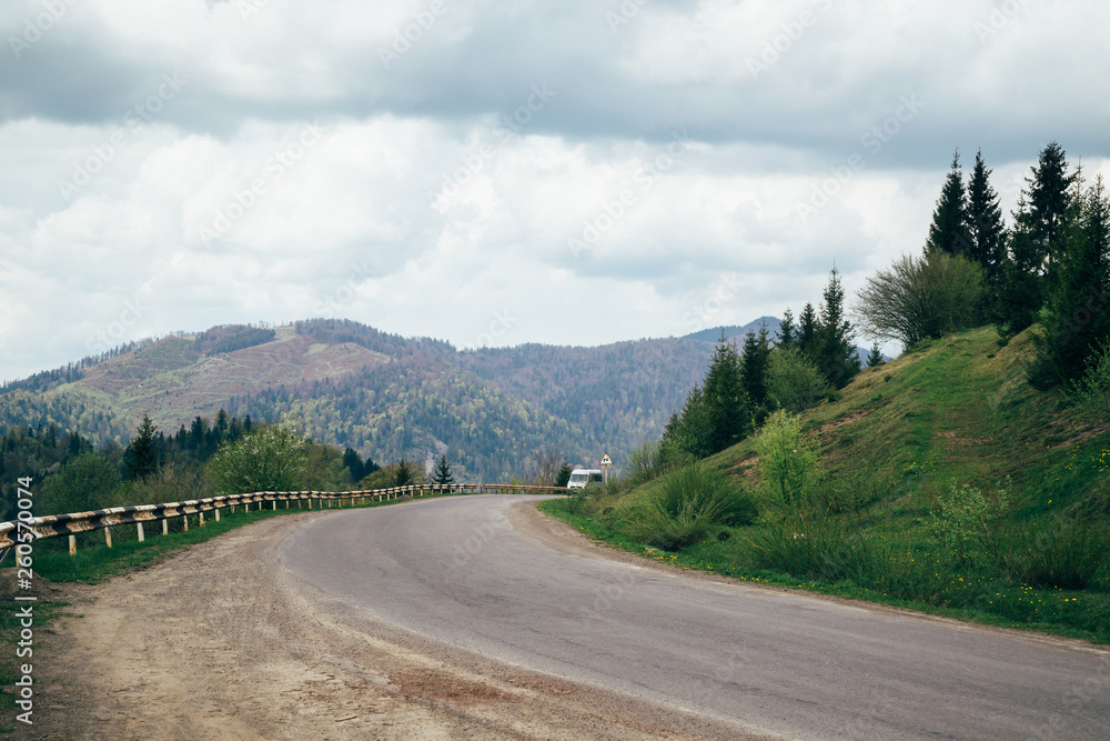 Old asphalt road and a car in the mountains with cloudy sky and forest on the background Old asphalt road and a car in the mountains with cloudy sky and forest on the background