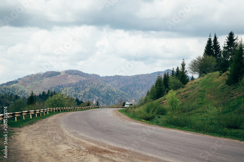 Old asphalt road and a car in the mountains with cloudy sky and forest on the background