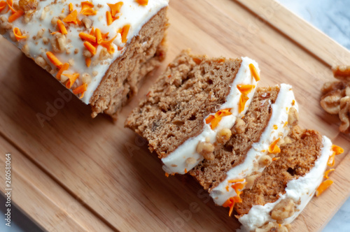 Loaf of carrot cake with cream cheese frosting and candy garnish on wooden table photo