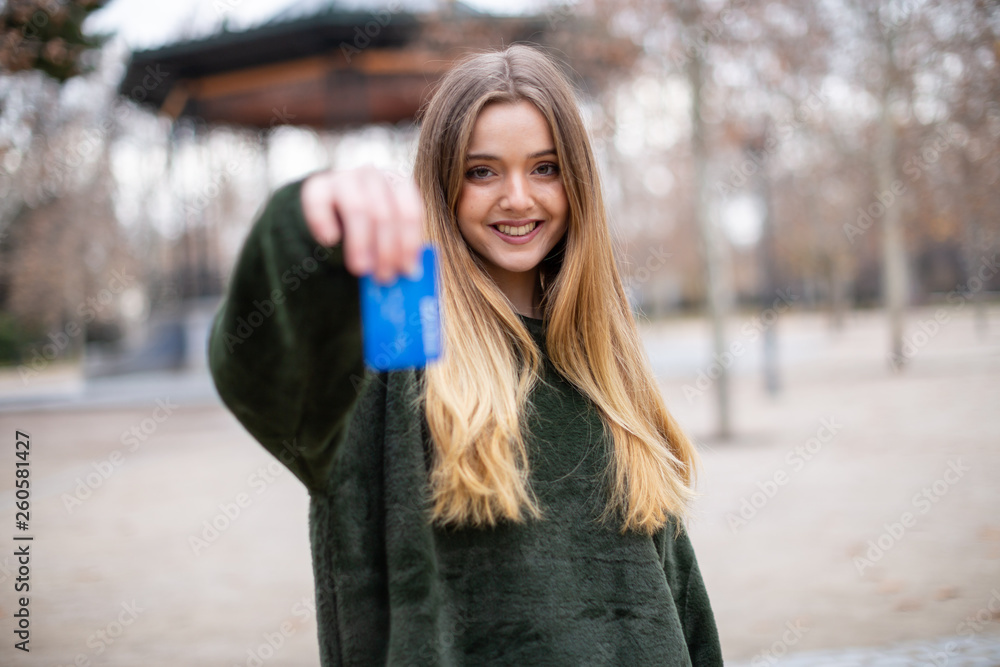Happy young lady with credit card while standing in park Happy young lady with credit card while standing in park