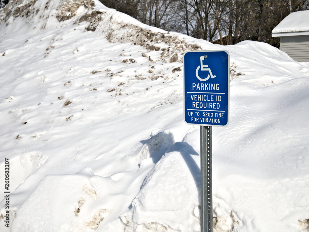 Handicapped parking sign in front of large pile snow parking lot in winter.