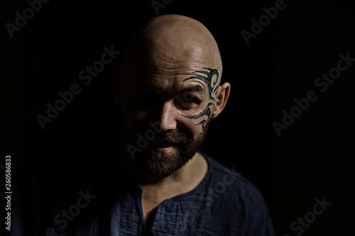 tattoo on the face   male portrait in the form of an assassin  cosplay   tattooed brutal man   guy with a tattooed face
