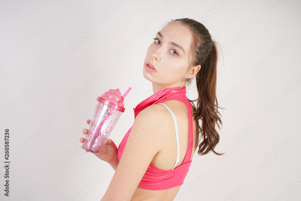 young beautiful caucasian teen girl in a pink short topic with a glass of water after training on a white background in the Studio young beautiful caucasian teen girl in a pink short topic with a glass of water after training on a white background in the Studio