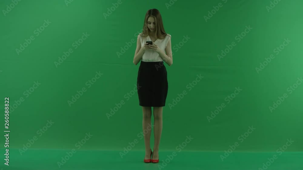 beautiful young business woman in white shirt and black skirt is using her mobile phone against green screen.