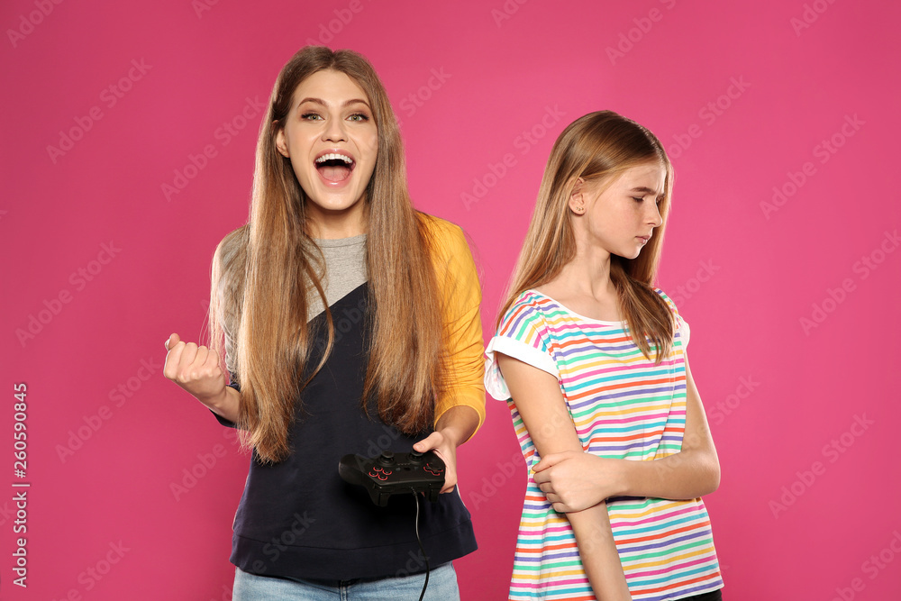 Young woman and teenage girl playing video games with controllers on color background Young woman and teenage girl playing video games with controllers on color background