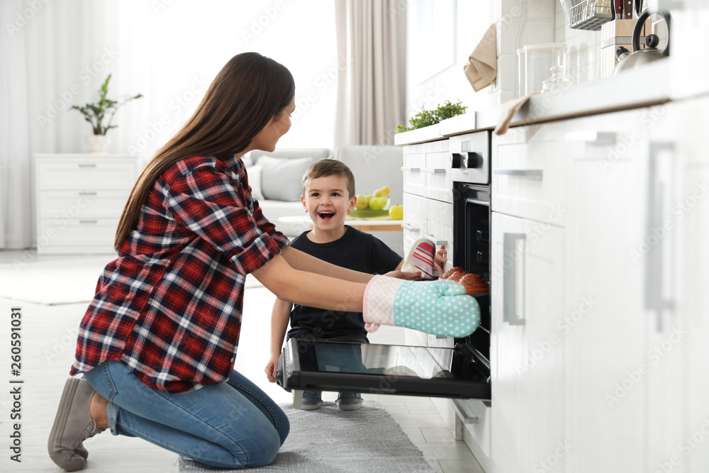 Son and mother taking out tray of baked buns from oven in kitchen Son and mother taking out tray of baked buns from oven in kitchen