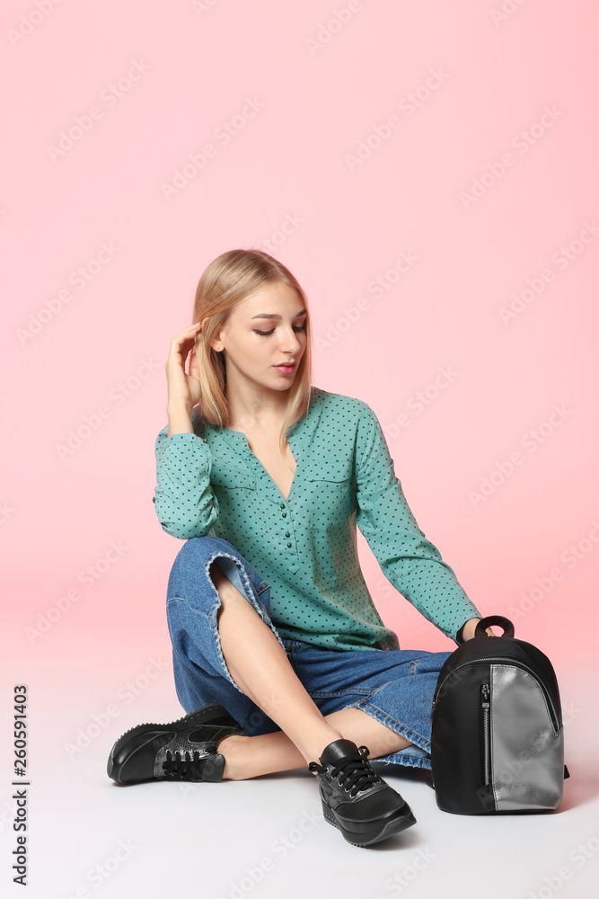 Fashionable young woman in stylish shoes with backpack sitting on color background Fashionable young woman in stylish shoes with backpack sitting on color background