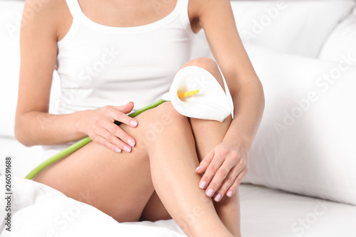 Young woman with perfect smooth skin holding calla flower on bed, closeup. Beauty and body care
