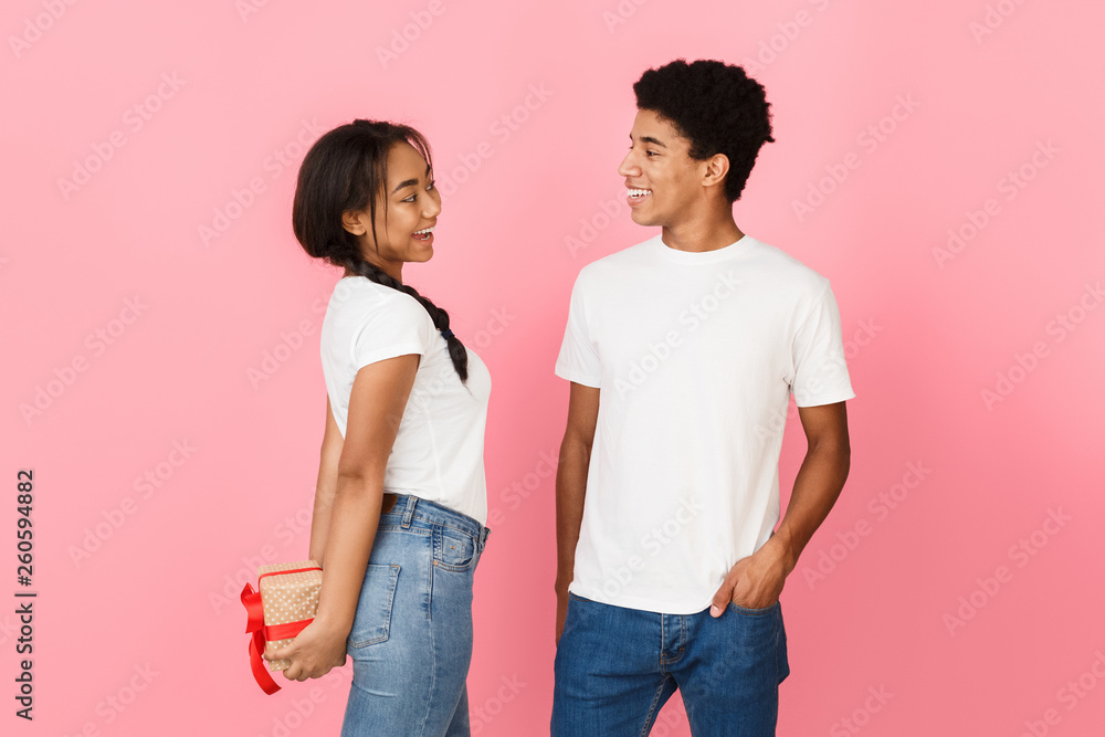 Girl hiding present from boyfriend, pink background Girl hiding present from boyfriend, pink background