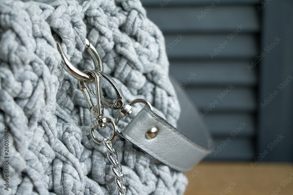 Extreme close-up of a handmade knitted bag in detail. Gray bag with leather bottom and straps.