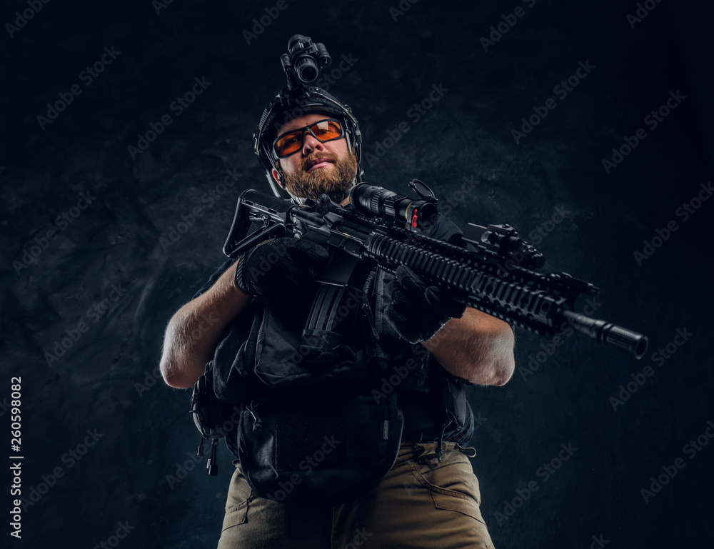 Special forces soldier wearing body armor and helmet with night vision holding an assault rifle. Studio photo against a dark textured wall Special forces soldier wearing body armor and helmet with night vision holding an assault rifle. Studio photo against a dark textured wall