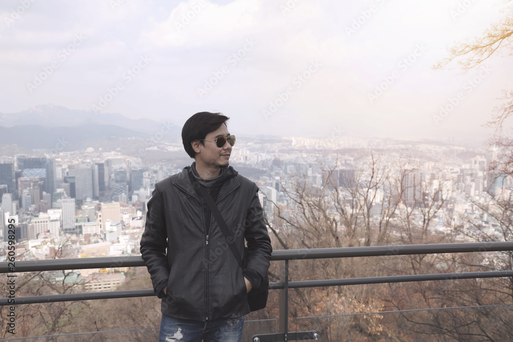 Fototapeta premium A man wearing sunglasses Black leather jacket And pale jeans Standing in the view point in winter