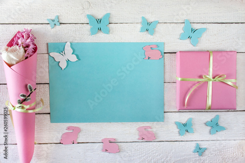 Pastelowe tło z niebieską kartką papieru, pudełkiem przewiązanym wstążką, kwiatami, motylami i zajączkami