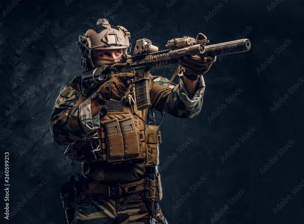 Fototapeta premium Elite unit, special forces soldier in camouflage uniform holding an assault rifle with a laser sight and aims at the target.