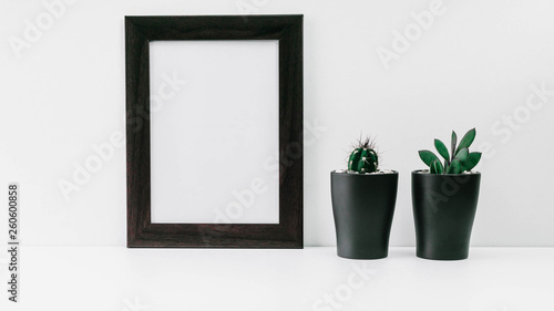 Empty dark photo frame and two succulents in dark pots on a white background. Scandinavian style MockUp © yusev
