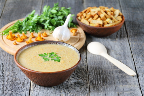 Chanterelle cream soup in a clay bowl on wooden background.