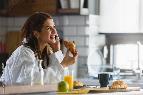 Young smiling woman in bathrobe just got up in the morning in the kitchen using smart phone