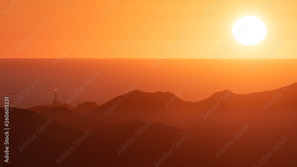 The lighthouse of Cabo de Palos and the Mediterranean Sea seen from afar behind the mountains of Calblanque at sunrise.