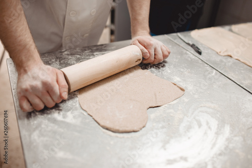 Baker is rolling dough on the table in the bakery
