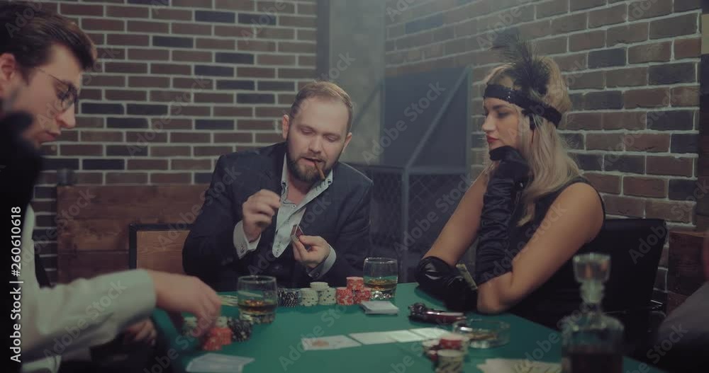 Man the player smokes a cigar, lets out a smoke. People are preparing to play a game of chance at the table. Man the player smokes a cigar, lets out a smoke. People are preparing to play a game of chance at the table.