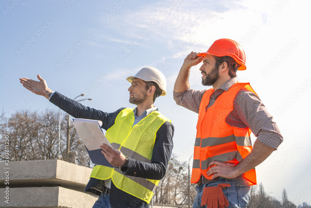 two men are builders workers are engineers at a construction site are looking at the drawings in helmets two men are builders workers are engineers at a construction site are looking at the drawings in helmets