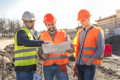 male builders workers engineers at a construction site looking drawings in helmets