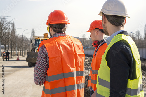 male workers engineers in helmets talking near the bulldozer and excavator